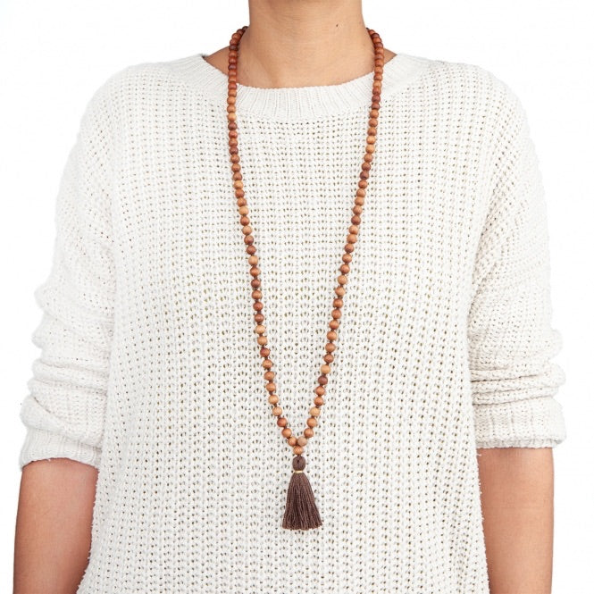 Mala in grani di legno di sandalo profumato, annodati singolarmente ad ogni grano, con nappine di colore marrone, indossato,