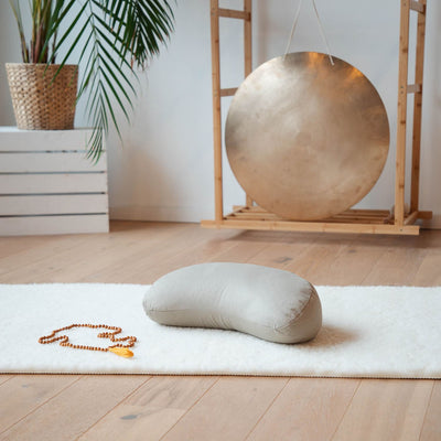 cuscino meditazione luna crescente color sabbia su tappetino yoga ecru con gong su sfondo 