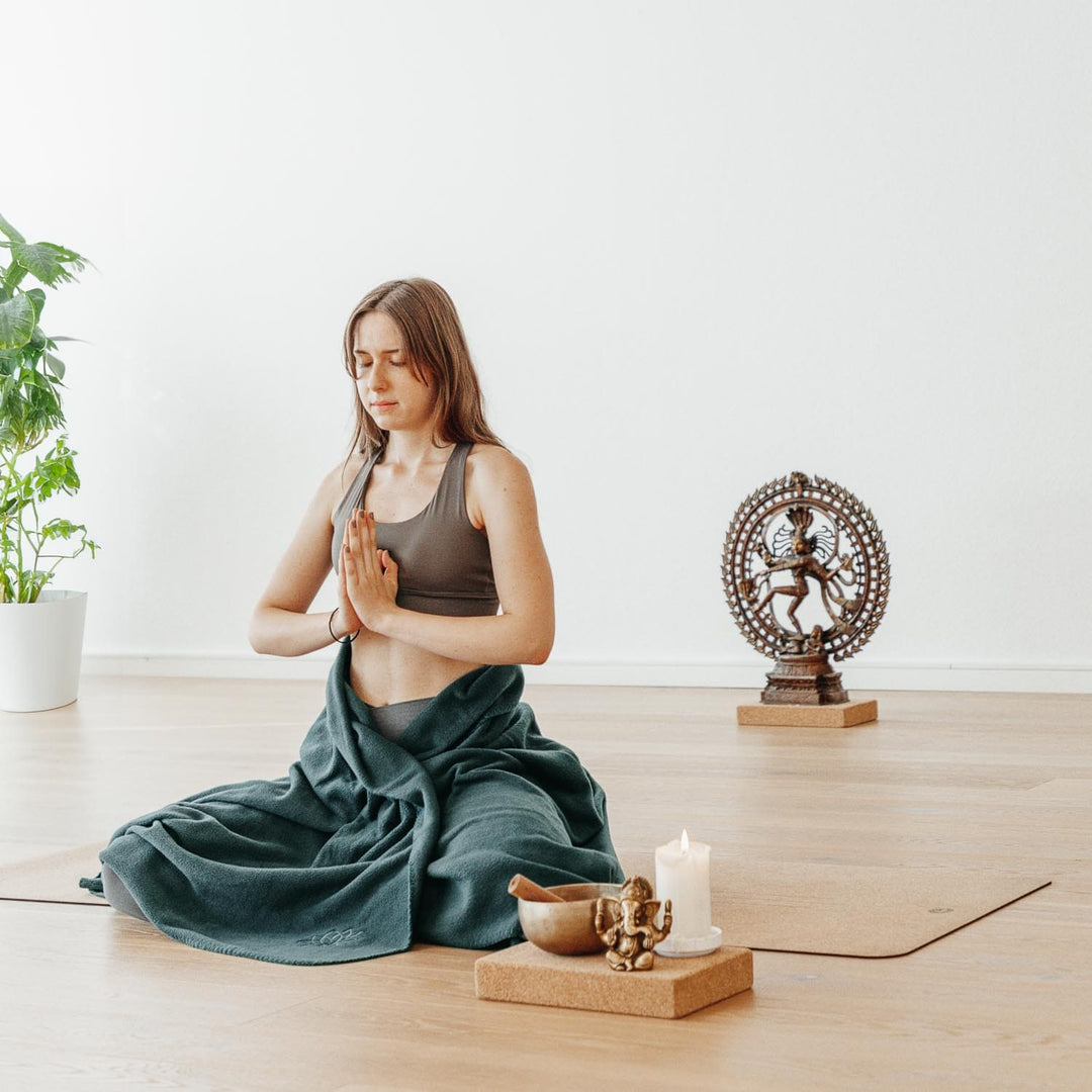 Modella che medita seduta gambe incrociate con addosso coperta asana verde foresta