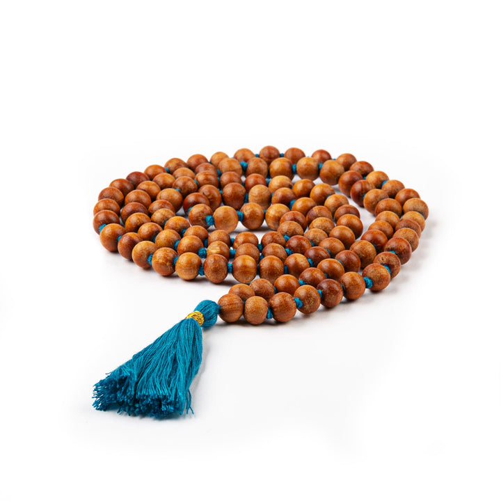 Mala in grani di legno di sandalo profumato, annodati singolarmente ad ogni grano, con nappine di colore azzurro, arrotolato