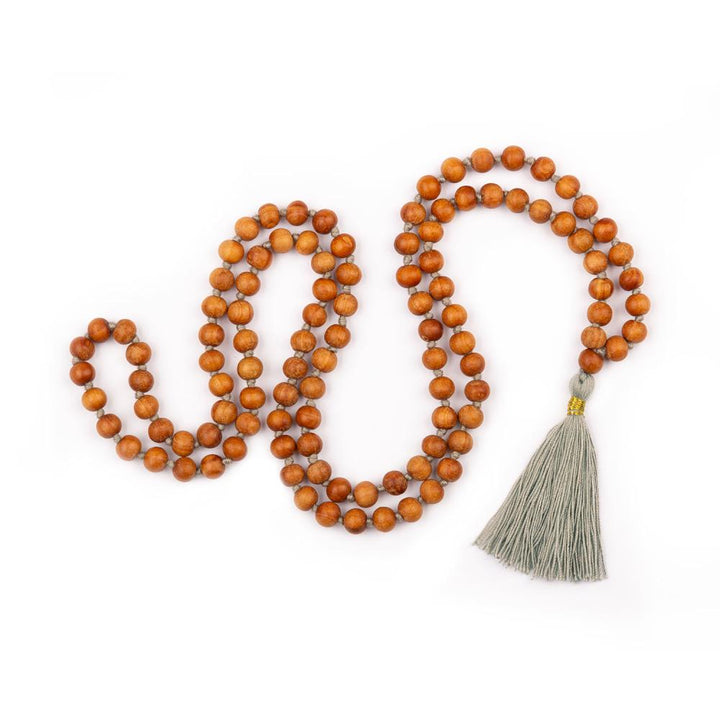 Mala in grani di legno di sandalo profumato, annodati singolarmente ad ogni grano, con nappine di colore grigio perla, disteso.